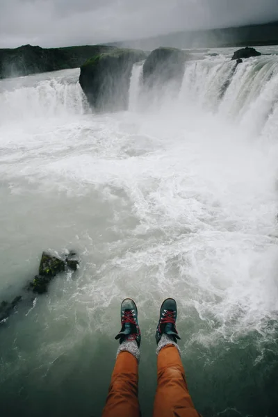 POV del hombre cuelgan las piernas del acantilado en la cascada — Foto de Stock