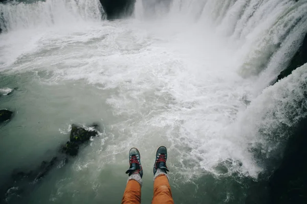 POV del hombre cuelgan las piernas del acantilado en la cascada —  Fotos de Stock