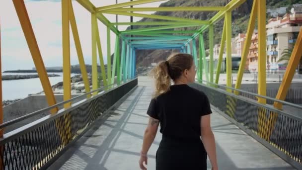 Junge hübsche Frau geht auf Regenbogenmetallbrücke — Stockvideo