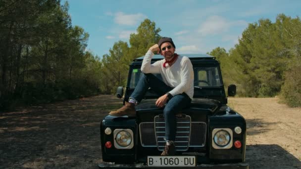 Hipster man sits on black adventure jeep in forest — Stock Video