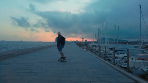 Jovem hipster homem no longboard na praia ao pôr do sol — Vídeo de Stock