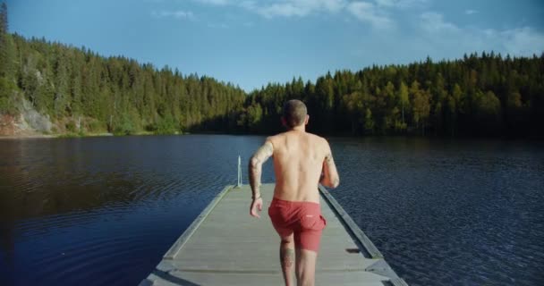 Чоловік біжить на причалі, щоб стрибнути в холодне гірське озеро — стокове відео