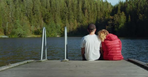 Χαριτωμένο ζευγάρι κάθονται σε ξύλινη αποβάθρα στη λίμνη δάσος — Αρχείο Βίντεο