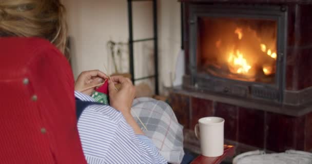 Vrouw breit rode wol wintersokken bij open haard — Stockvideo