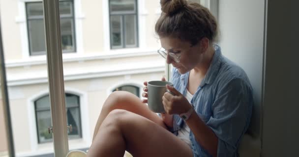 Jeune femme en pyjama confortable boire du café sur le balcon — Video