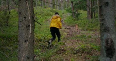 Genç bir kadın köpeğiyle orman yolunda koşuyor.