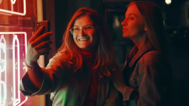 Dwa tysiąclecia kobiety pozować na aparat fotograficzny w neon — Wideo stockowe