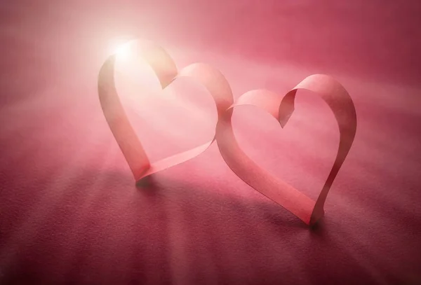two beautiful romantic heart, made of paper tape in the rays of light on a red paper background - pictures concept theme love and St. Valentine's Day
