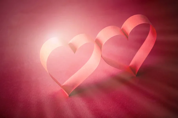 two beautiful romantic heart, made of paper tape in the rays of light on a red paper background - pictures concept theme love and St. Valentine\'s Day