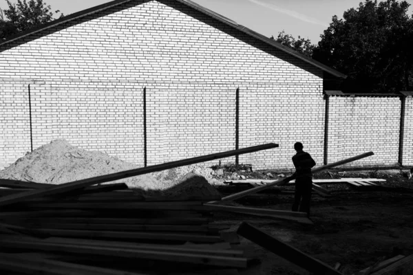 Um trabalhador descarrega na construção de tábuas de madeira em um backg — Fotografia de Stock