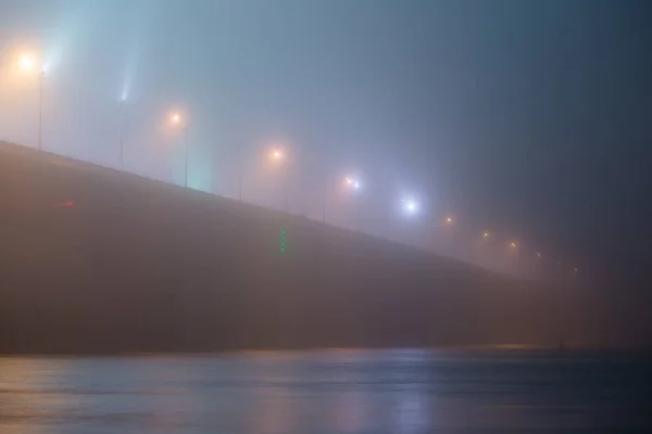 Uma noite misteriosa neblina acima do rio na cidade grande. Ponte em — Fotografia de Stock