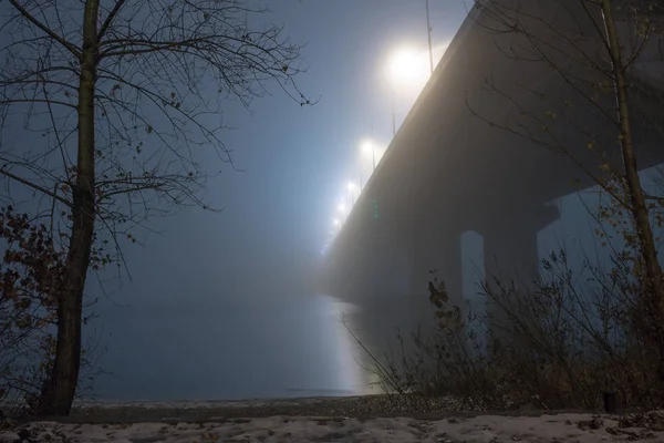 Een mysterieuze avond mist boven de rivier in de grote stad. Brug in — Stockfoto