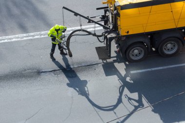 Yol yüzeyi yenileme işi. İşçi, asfalt yüzeyindeki zift emülsiyonu ve kuru toplamla kaplanarak çatlakların onarımı ve kapatılması üzerinde yol yamacıda çalışır..