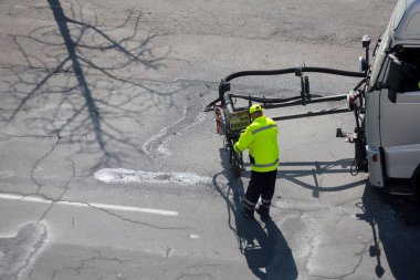 Yol yüzeyi yenileme işi. İşçi, asfalt yüzeyindeki zift emülsiyonu ve kuru toplamla kaplanarak çatlakların onarımı ve kapatılması üzerinde yol yamacıda çalışır..