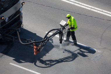 Yol yüzeyi yenileme işi. İşçi, asfalt yüzeyindeki zift emülsiyonu ve kuru toplamla kaplanarak çatlakların onarımı ve kapatılması üzerinde yol yamacıda çalışır..