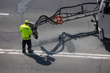 Yol yüzeyi yenileme işi. İşçi, asfalt yüzeyindeki zift emülsiyonu ve kuru toplamla kaplanarak çatlakların onarımı ve kapatılması üzerinde yol yamacıda çalışır..