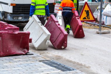 Asfalt inşaatı. Kaldırıma beton kaldırım taşları yerleştirildi. İşçiler plastik yol bariyerlerini sürüklüyor.