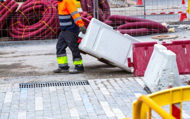 Asfalt inşaatı. İşçiler plastik yol bariyerlerini sürüklüyor. Arka plandaki yeraltı mühendisliği iletişimi için plastik borular..