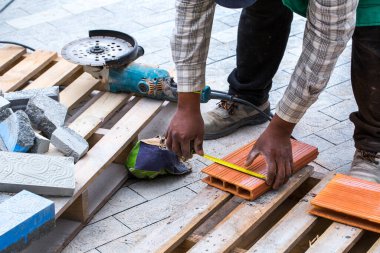 Asfalt inşaatı. Kaldırıma beton kaldırım taşları yerleştirildi. Bir işçi disk kesiciyle ölçümler yapar, işaretler ve keser..