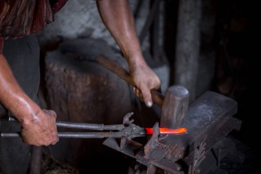 Demircinin elleri iş başında. Bir elinde çekiç, diğer elinde sıcak metalden bir iş parçası. Usta düzenli olarak örse vuruyor. Eski el sanatlarının sıkı çalışmasına bir örnek..