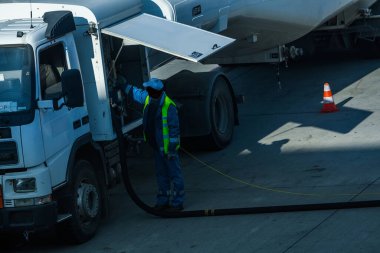 Havaalanının bir çalışanı tankeri çalıştırıyor ve uçağı havacılık yakıtıyla dolduruyor..