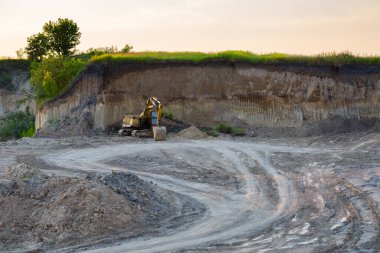 Kazıcı, küçük bir tuğla fabrikasının kil ocağında duruyor. Endüstriyel alanda akşam güneşi.