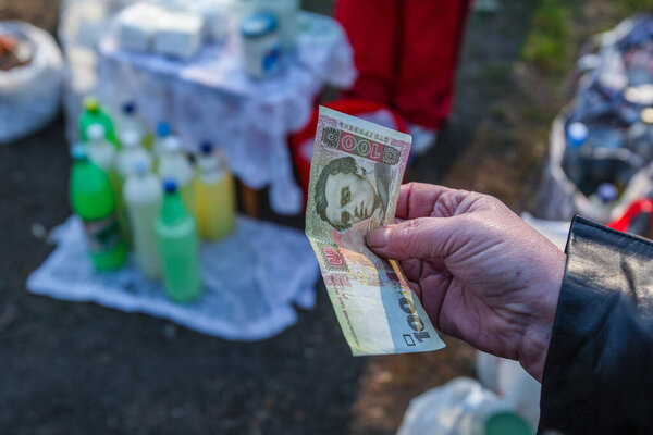 Воскресная ярмарка в небольшом селе в центральной Украине Черкасской области. Лицо покупателя крестьянин держит в руке банкноту в размере 100 грн. Молоко в ПЭТ бутылки.