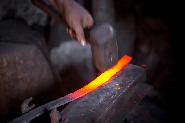 铁匠的手在工作 一只手拿着锤子 另一只手拿着热金属的工件 主人有条不紊地把铁锤打在铁锤上 古代手工艺品勤劳劳动的一个例子 — 图库照片