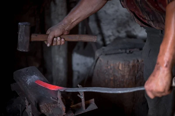 铁匠的手在工作 一只手拿着锤子 另一只手拿着热金属的工件 主人有条不紊地把铁锤打在铁锤上 古代手工艺品勤劳劳动的一个例子 — 图库照片