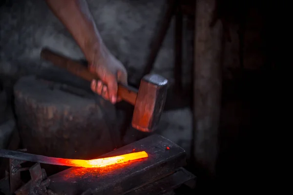 Blacksmith\'s hands at work. In one hand a hammer, in the other a workpiece of hot metal. Master methodically hammer hits the anvil. An example of the hard work of ancient crafts.