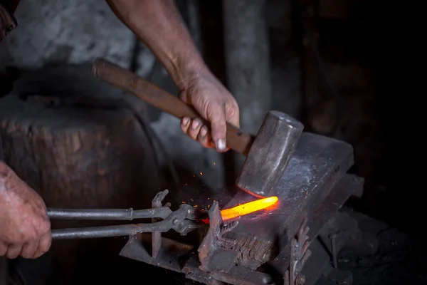 Blacksmith\'s hands at work. In one hand a hammer, in the other a workpiece of hot metal. Master methodically hammer hits the anvil. An example of the hard work of ancient crafts.