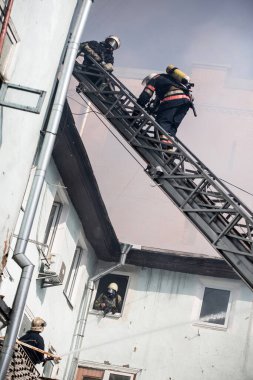 Oksijen maskeli merdivenlerdeki itfaiyeciler şehrin ortasındaki eski bir evde çıkan yangını söndürüyor.