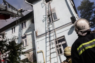 Oksijen maskeli merdivenlerdeki itfaiyeciler şehrin ortasındaki eski bir evde çıkan yangını söndürüyor.