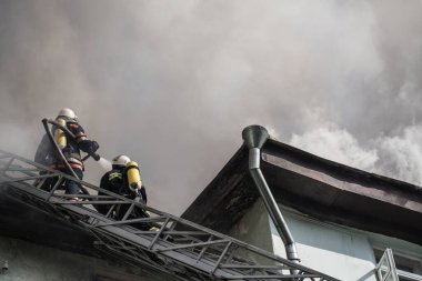 Oksijen maskeli merdivenlerdeki itfaiyeciler şehrin ortasındaki eski bir evde çıkan yangını söndürüyor.