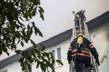 Oksijen maskeli merdivenlerdeki itfaiyeciler şehrin ortasındaki eski bir evde çıkan yangını söndürüyor.