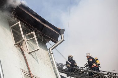 Oksijen maskeli merdivenlerdeki itfaiyeciler şehrin ortasındaki eski bir evde çıkan yangını söndürüyor.