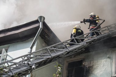 Oksijen maskeli merdivenlerdeki itfaiyeciler şehrin ortasındaki eski bir evde çıkan yangını söndürüyor.