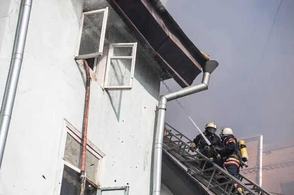 燃烧的碎片从屋顶下掉下来 身着氧气面罩的消防员在梯子上扑灭了市中心一幢老房子的大火 — 图库照片
