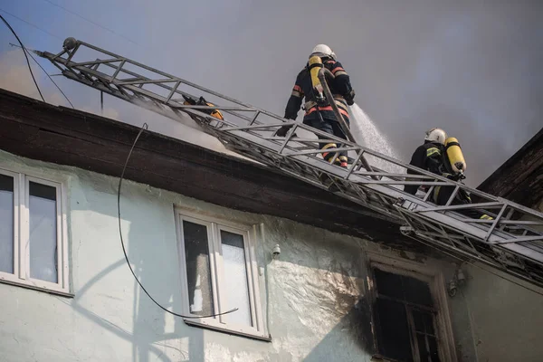 身着氧气面罩的消防员在梯子上扑灭了市中心一幢老房子的大火 — 图库照片