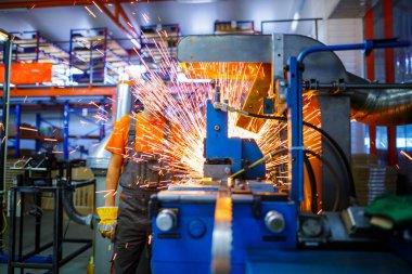 Metal ürünlerinin endüstriyel üretiminde kaynak makinesi üzerinde çalışan erkek bir tamirci. Parçaların altından kıvılcımlar çıkıyor. Konsept tema onarımı, mekanik, üretim, endüstri. Tanımlanamayan yüz