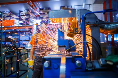Metal ürünlerinin endüstriyel üretiminde kaynak makinesi üzerinde çalışan erkek bir tamirci. Parçaların altından kıvılcımlar çıkıyor. Konsept tema onarımı, mekanik, üretim, endüstri. Tanımlanamayan yüz