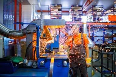 Metal ürünlerinin endüstriyel üretiminde kaynak makinesi üzerinde çalışan erkek bir tamirci. Parçaların altından kıvılcımlar çıkıyor. Konsept tema onarımı, mekanik, üretim, endüstri. Tanımlanamayan yüz