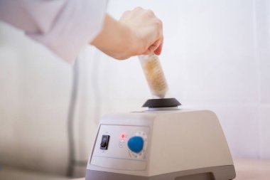 Laboratuvar bilimcisi, laboratuvar girdabı mikseri üzerinde analiz için biyolojik örneği ayarlanabilir karıştırma hızıyla dokunuş hızını karıştırıyor..
