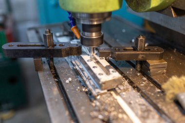 Çalışma sürecinin endüstriyel bir değirmen makinesinde yürütülmesi. Metal kısım kolona kenetlenmiş. Kesici boylamsal bir oyuk oluşturuyor. Soğutucu tedarik edildi. Metal talaşları kenarlara doğru uçar..