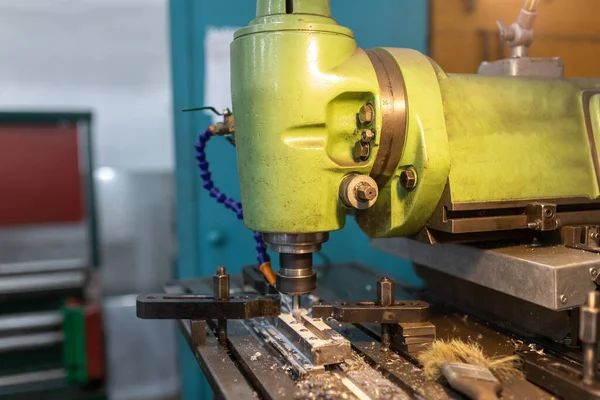 Execution of the work process on an industrial milling machine. The metal part is clamped in the collet. The cutter makes a longitudinal groove. Coolant is supplied. Metal shavings fly to the sides.