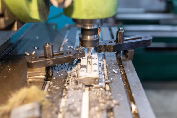 Execution of the work process on an industrial milling machine. The metal part is clamped in the collet. The cutter makes a longitudinal groove. Coolant is supplied. Metal shavings fly to the sides.