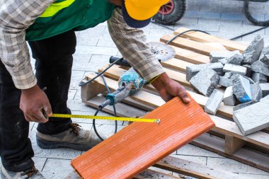 Asfalt inşaatı. Kaldırıma beton kaldırım taşları yerleştirildi. Bir işçi disk kesiciyle ölçümler yapar, işaretler ve keser..