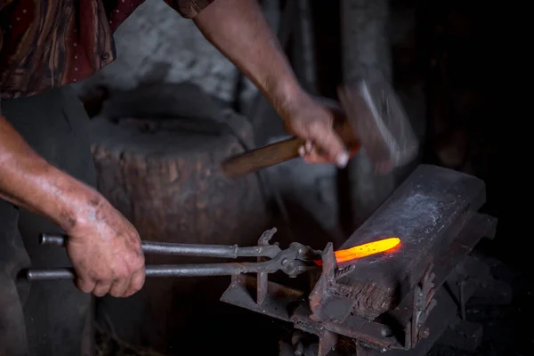 Blacksmith\'s hands at work. In one hand a hammer, in the other a workpiece of hot metal. Master methodically hammer hits the anvil. An example of the hard work of ancient crafts.