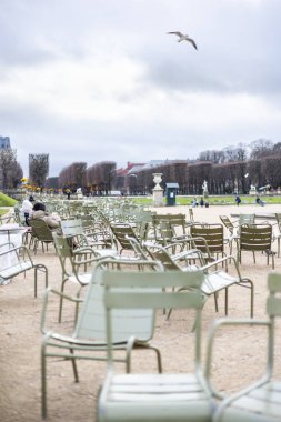 Lüksemburg Bahçeleri, Paris, Fransa 'da çakıl yolunda birden fazla açık yeşil metal sandalye. Bulutlu bir sonbahar gününde arka planda tanınmayan insanlar görünür..
