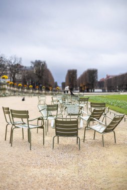 Lüksemburg Bahçeleri, Paris, Fransa 'da çakıl yolu üzerinde çok sayıda açık yeşil metal sandalye ve bulutlu bir sonbahar gününde arka planda uzun bir ağaç gezinti..